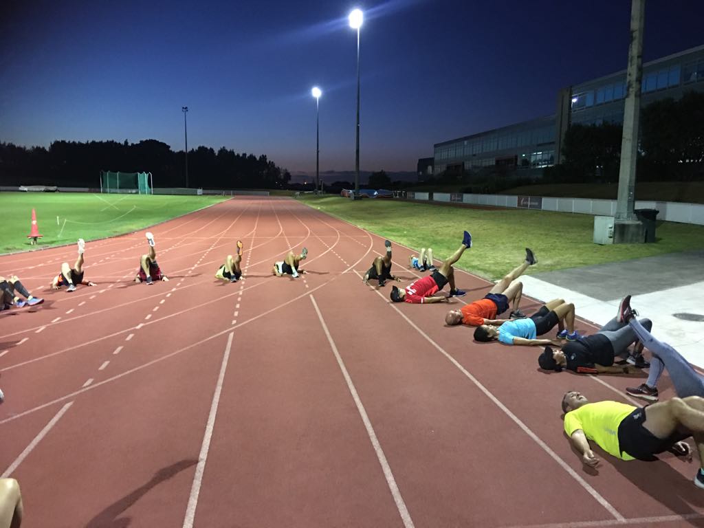 A collection of runners on the AUT Millennium running track lying down to perform glute bridges.